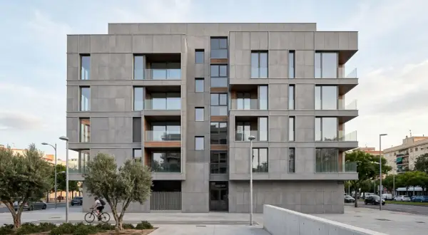 Edificio moderno con una elegante fachada ventilada de paneles grises, balcones acristalados y detalles en madera. Un ciclista pasa frente a árboles y la calle.