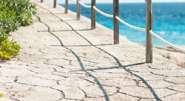 Camino de piedra con barandilla y mar azul. Un ejemplo de cómo hacer hormigón impreso para exteriores.