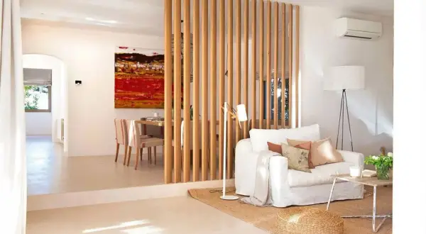 Elegante separador de madera para dividir salón en dos ambientes. Sofá blanco, mesa de centro rústica y cuadro vibrante.