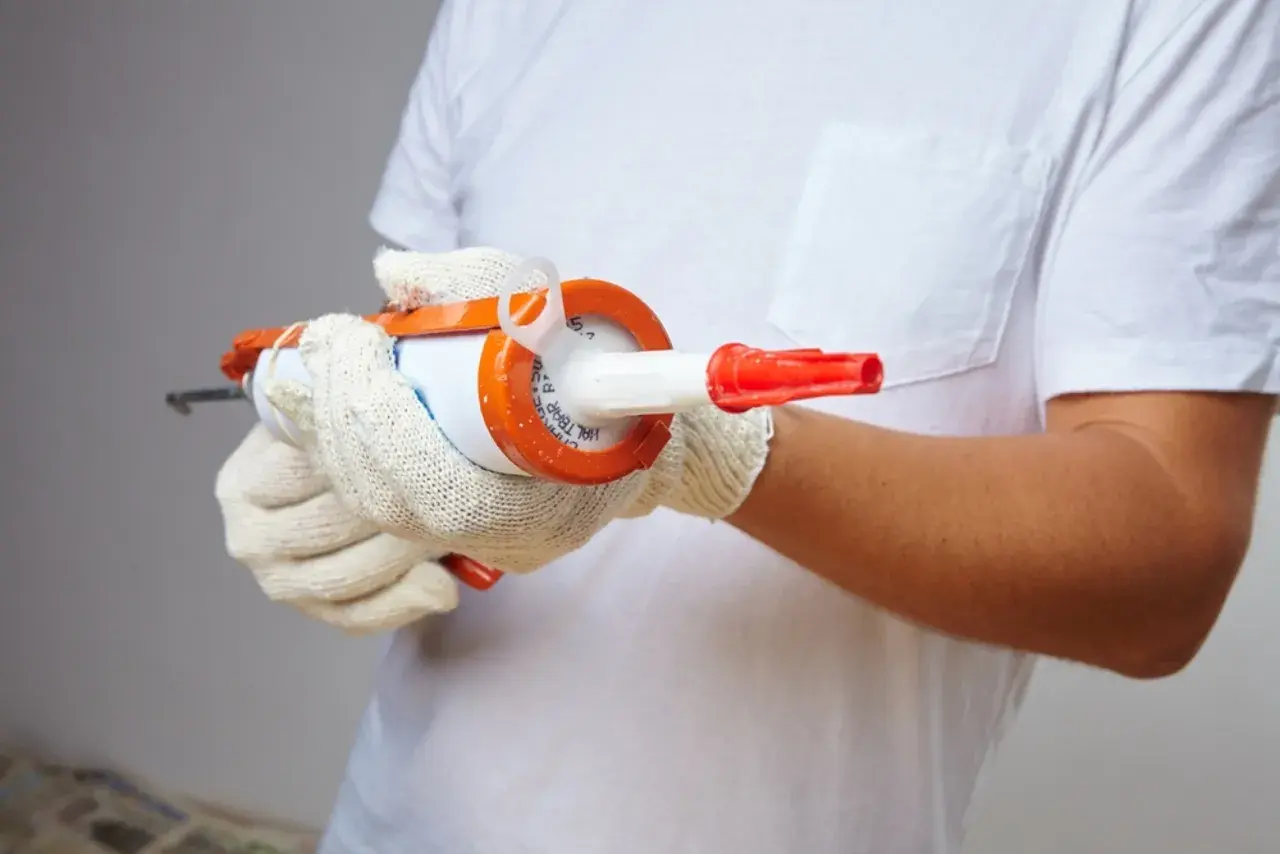 Manos enguantadas sujetan pistola de silicona, preparándose para sellar. ¿Cuánto tarda en secar la silicona?