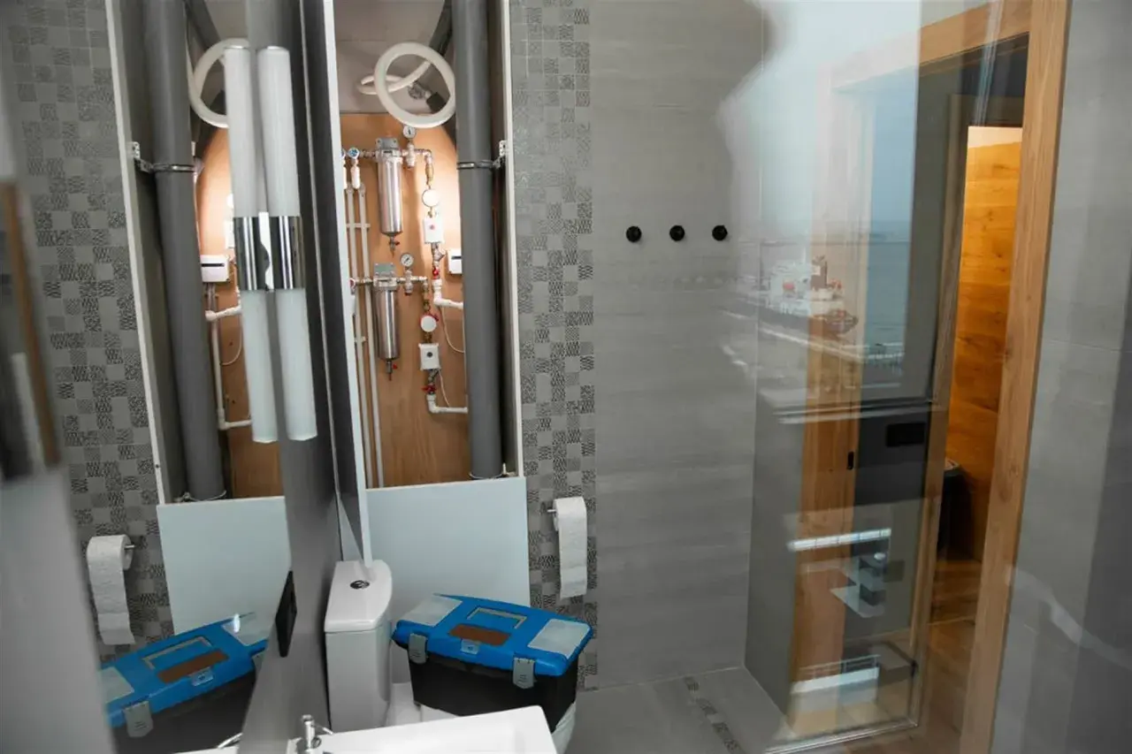 Herramientas listas para instalar mampara ducha esquina. Baño moderno con tuberías visibles y vista al mar.