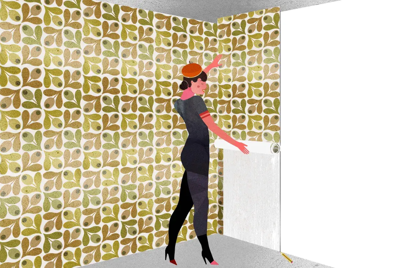 Una mujer con boina naranja y vestido gris está aprendiendo cómo empapelar una pared con un patrón de hojas y olivas.