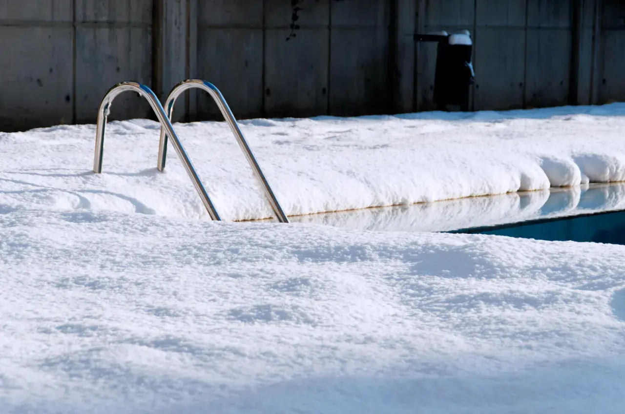Escaleras de piscina asoman entre la nieve. Un reto para mantener piscina en invierno sin tapar.