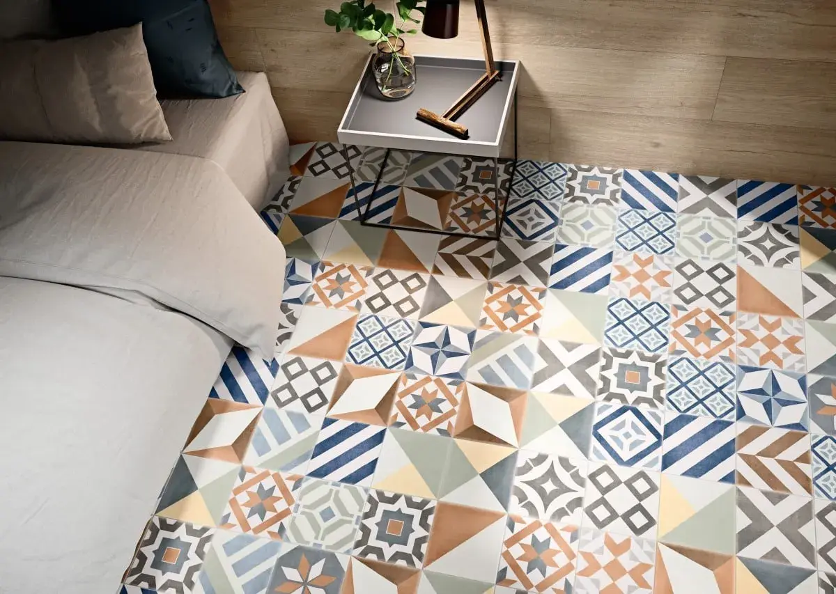 Un suelo con **baldosa hidráulica** de diseño geométrico y colores vibrantes, junto a una cama y una mesita de noche.
