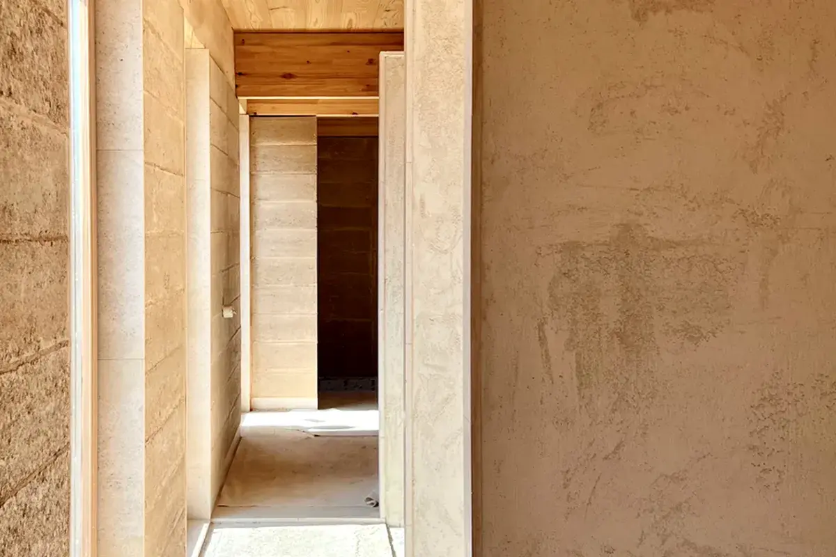 Pasillo con paredes de mortero de cal interiores, textura natural y vigas de madera en el techo.