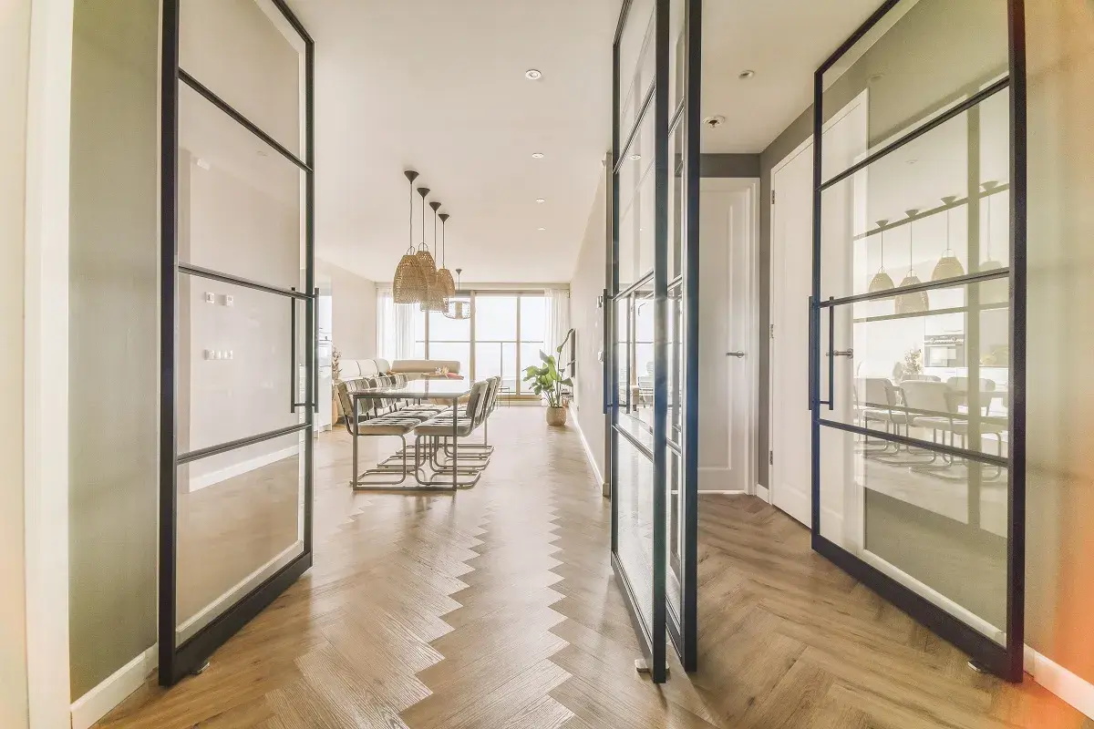 Amplio salón comedor rectangular de 25 metros, con suelo de espiga y separadores de cristal.