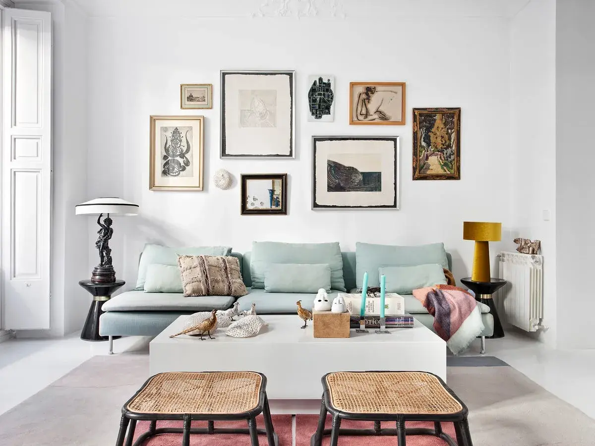 Un sofá azul claro con cojines decorativos y una colección de arte ecléctica en la pared. Ideas de qué poner detrás del sofá: una galería de arte o una estantería.