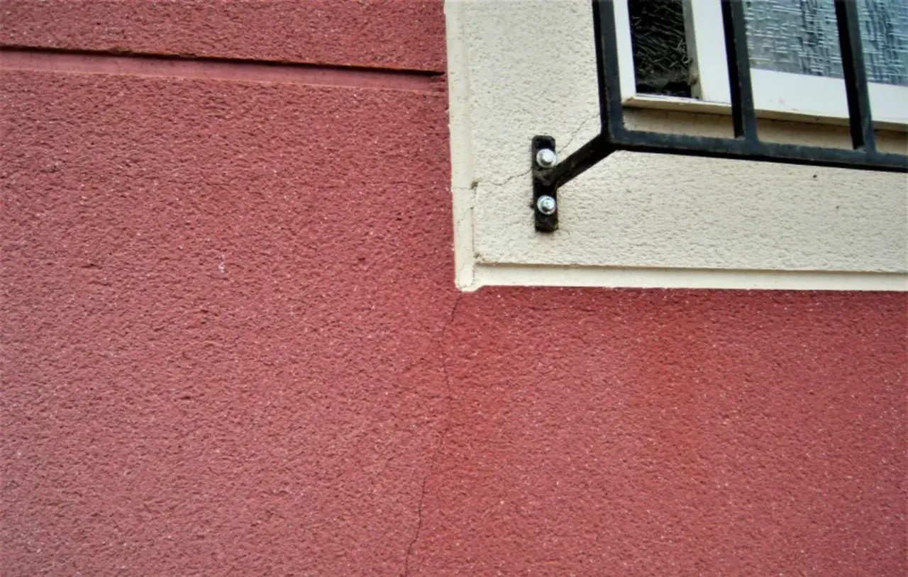 Detalle de juntas de dilatación en fachadas de color rojo y crema, con una ventana enrejada.