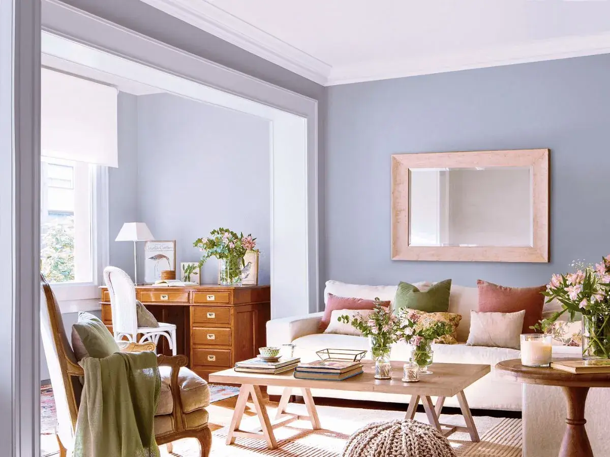 Ideas para decorar casa con poco dinero: sala acogedora con escritorio de madera, sofá blanco, cojines coloridos y flores frescas.