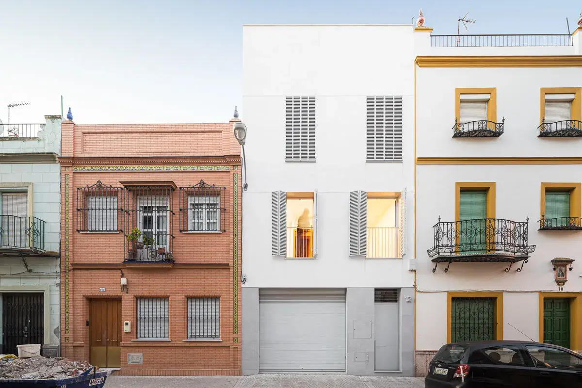 Fachada edificio con ladrillo visto y detalles de azulejos, junto a una moderna construcción blanca y otra amarilla con balcones de forja.