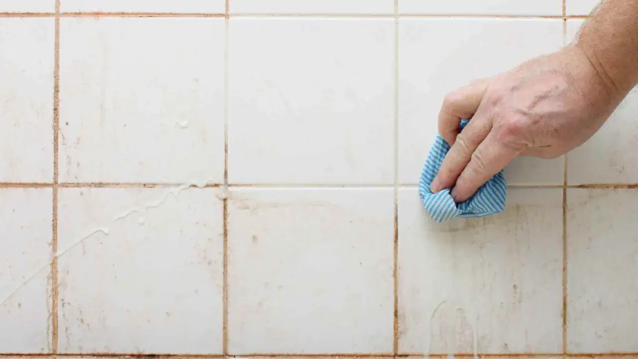 Mano limpiando juntas de azulejos sucias con un paño azul.