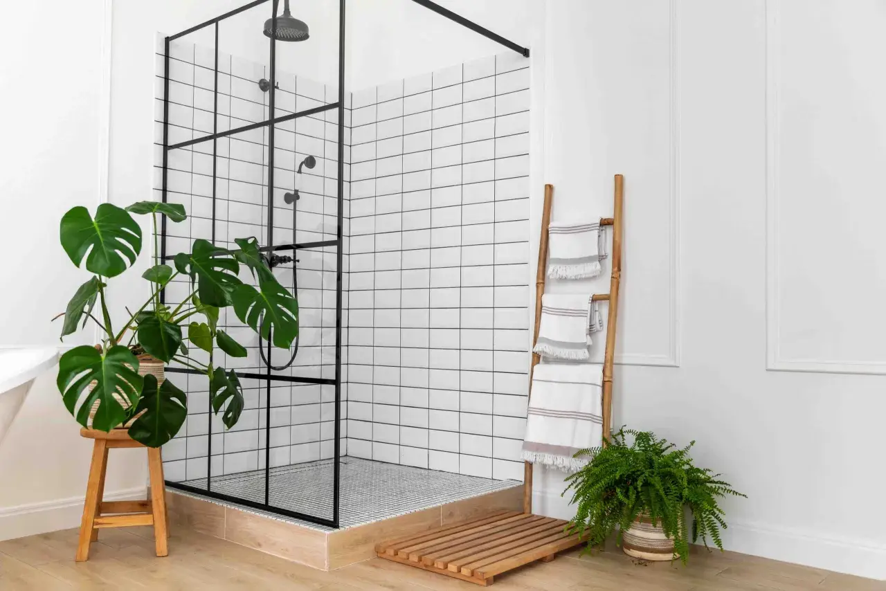 Un plato de ducha moderno con mampara negra, azulejos blancos y plantas. Ideal para saber como poner un plato de ducha.