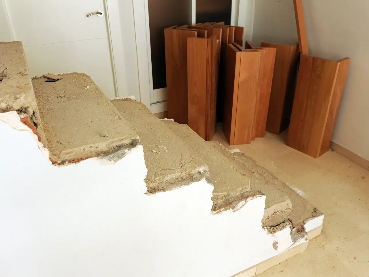Preparativos para revestir escalera antigua. Tablas de madera apiladas junto a escalones de hormigón en proceso de reforma.