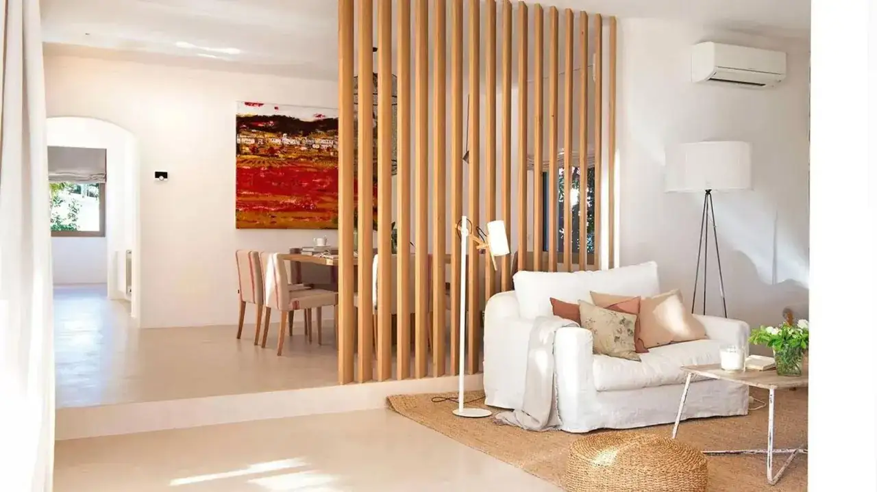 Elegante separador de madera para dividir salón en dos ambientes. Sofá blanco, mesa de centro rústica y cuadro vibrante.