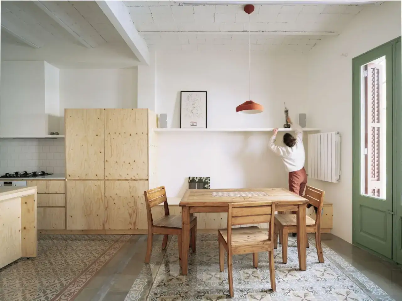 Comedor con suelo de baldosa hidr&aacute;ulica, muebles de madera contrachapada y una persona ajustando una estanter&iacute;a.