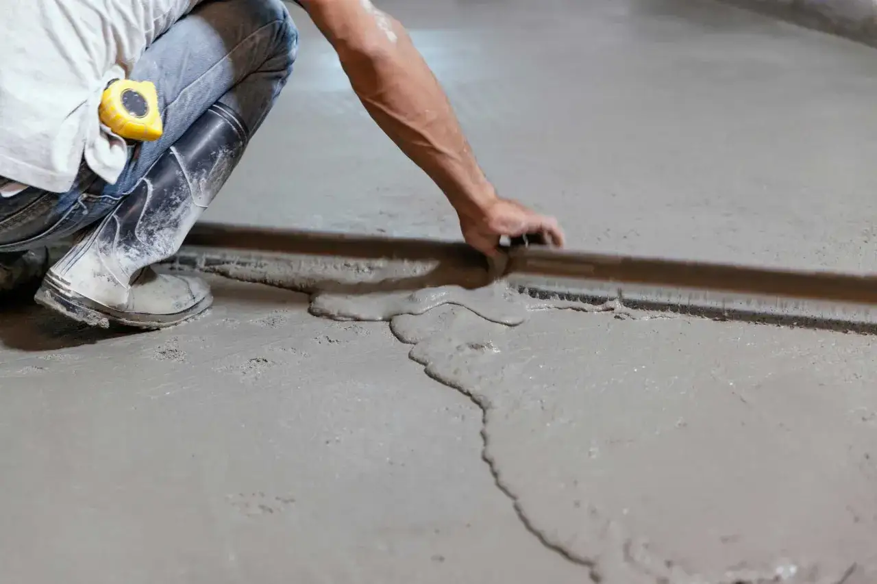 Obrero trabajando en como nivelar un suelo de cemento, usando una regla de albañil para esparcir el material fresco.