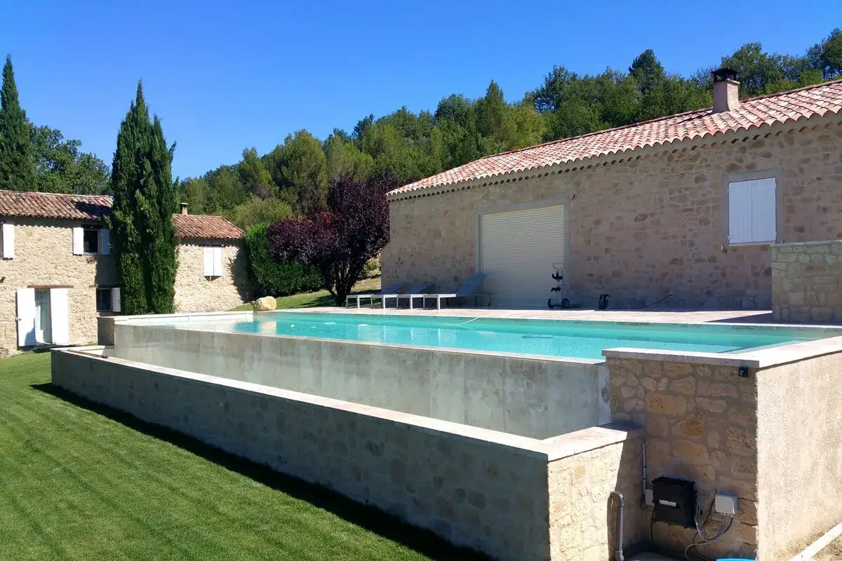 Piscina elevada de hormig&oacute;n y piedra, con c&eacute;sped y casas de campo. Ideal para aprender como hacer una alberca elevada.