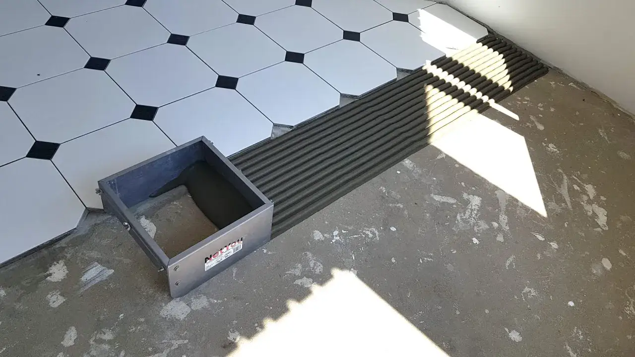 Colocación de baldosas con cemento cola. Se ve una llana dentada esparciendo el material sobre el suelo.