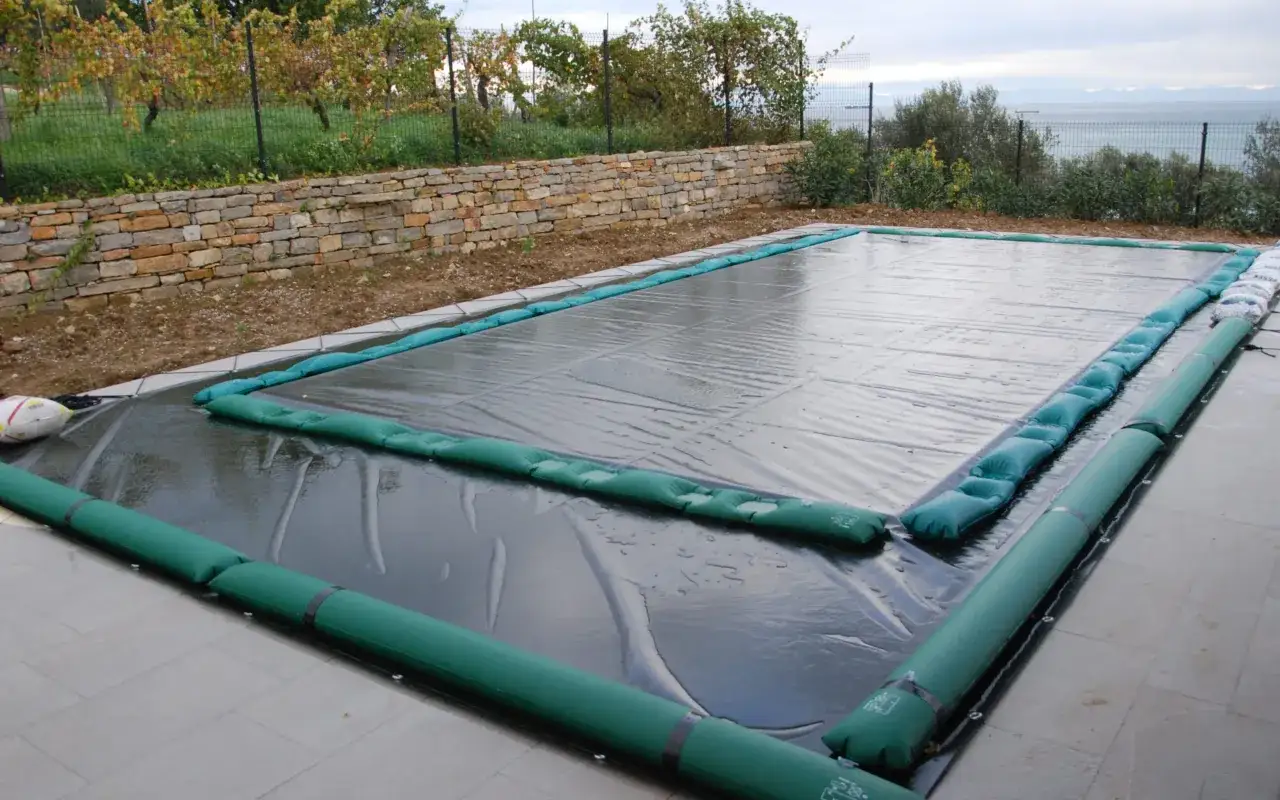 Cubierta de piscina para el invierno, con flotadores verdes y una pelota de rugby.