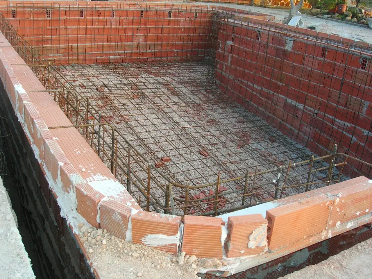 Construcci&oacute;n de una piscina de obra: paredes de ladrillo y armadura de hierro listas para el hormig&oacute;n.