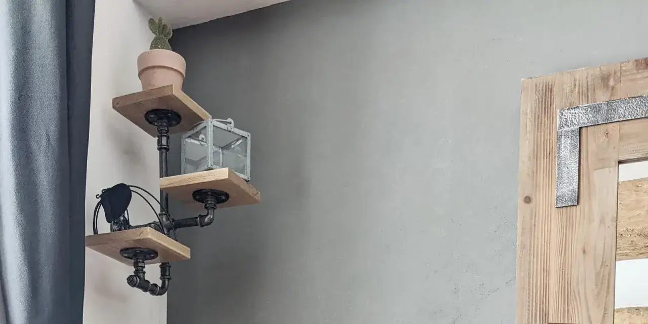 Estantes DIY de madera y tuber&iacute;a industrial con un cactus, linterna y un objeto negro.