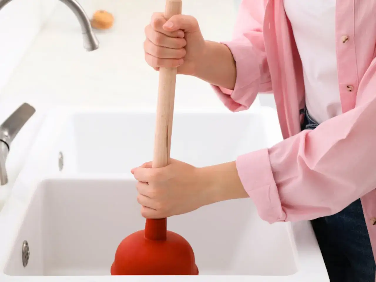 Persona usa un desatascador rojo para como desatascar un lavabo.