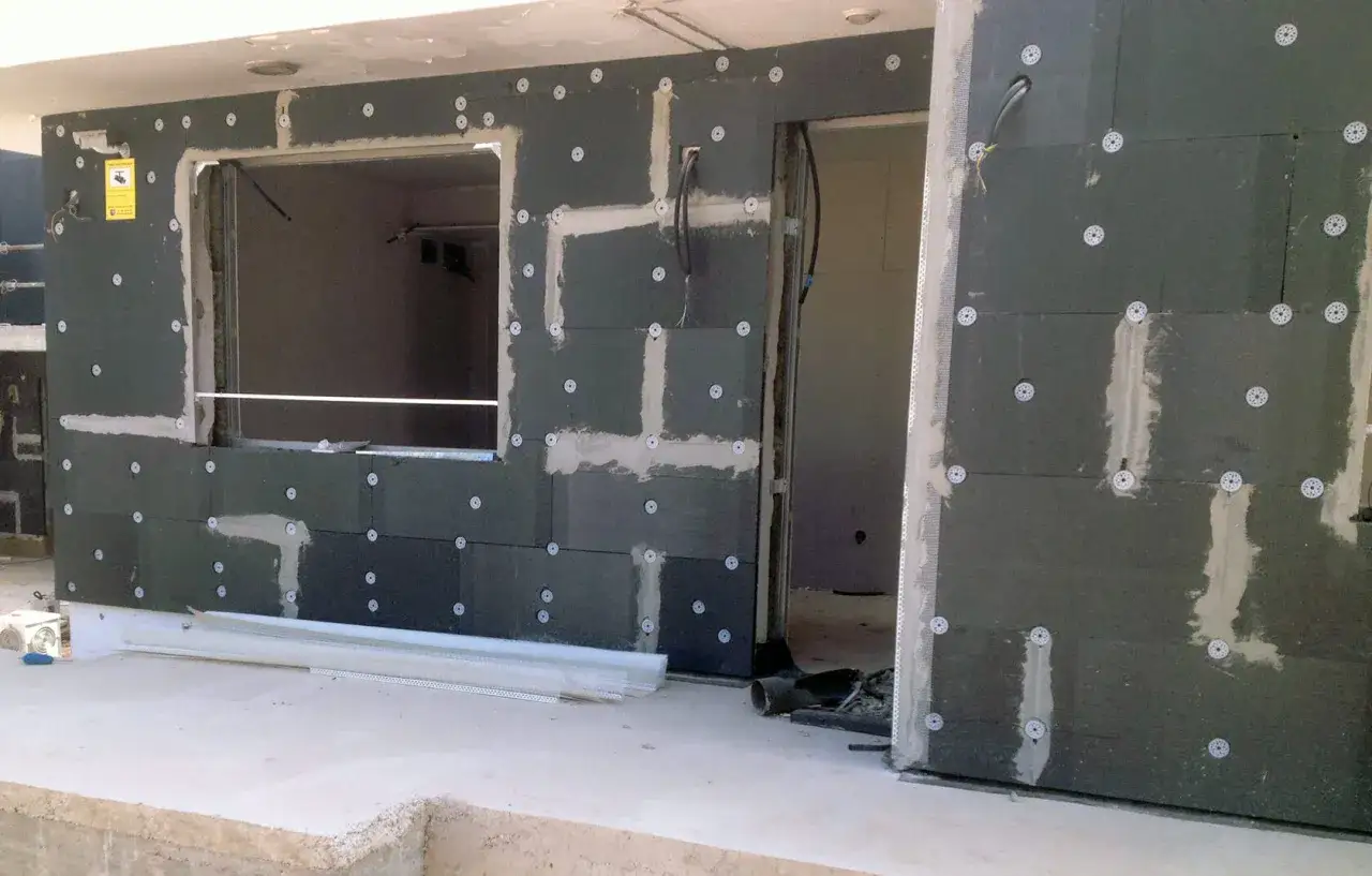 Fachada en construcci&oacute;n con mortero aplicado sobre poliestireno extruido, fijado con discos. Se aprecian huecos para ventana y puerta.
