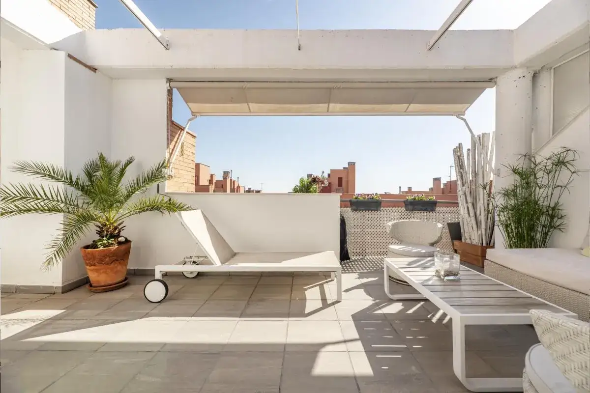 Elegante decoracion terrazas aticos con tumbona, mesa de centro y plantas. Un oasis de paz en la azotea.