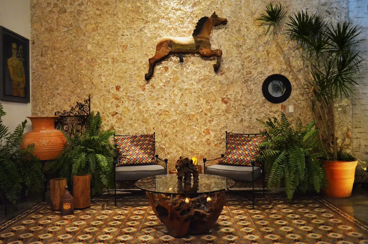 Un caballo decorativo adorna la pared de un patio exterior, junto a plantas y muebles acogedores.