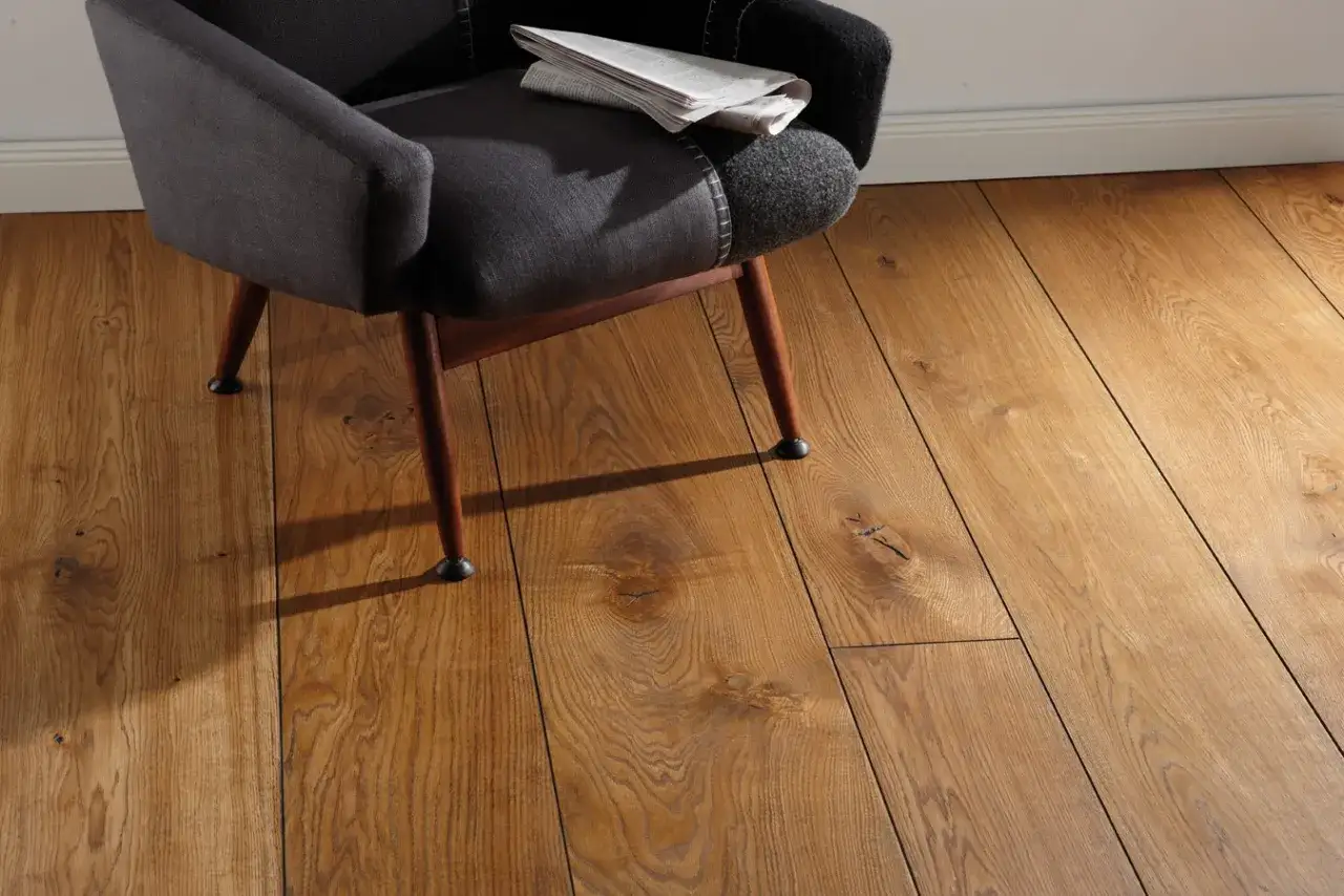 Silla oscura sobre un cálido suelo laminado o parquet de madera con nudos visibles.