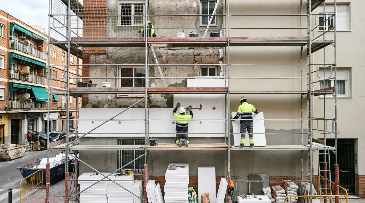 Obreros instalan aislamiento térmico en sate fachadas. Andamios rodean el edificio en construcción.