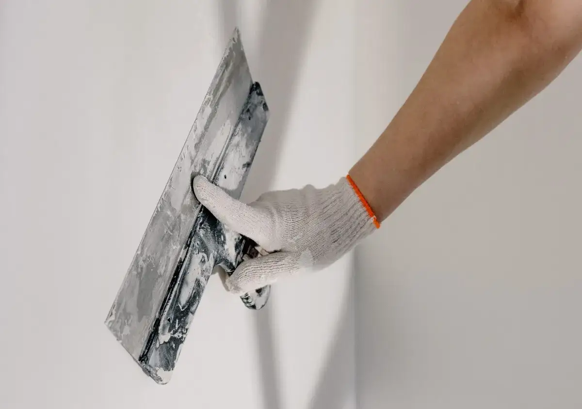 Mano con guante blanco aplicando cemento cola con llana para poner azulejos.