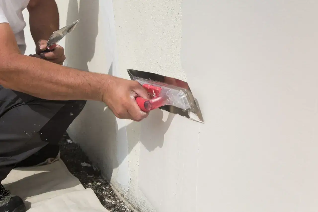 Man aplicando revoco con llana, alisando la pared para un acabado perfecto.
