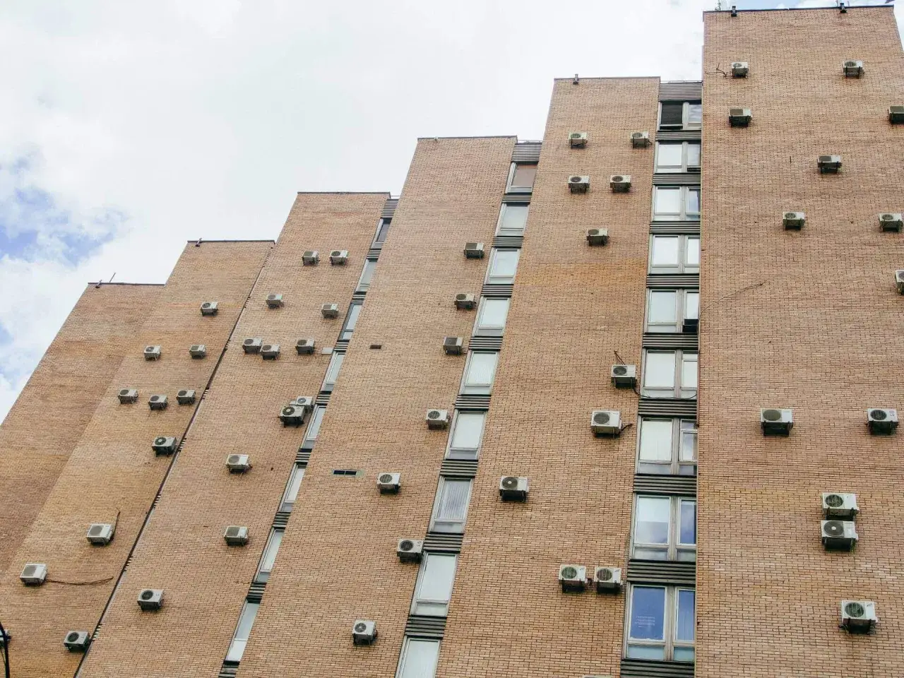 Fachada exterior de edificio de ladrillo con múltiples unidades de aire acondicionado instaladas.