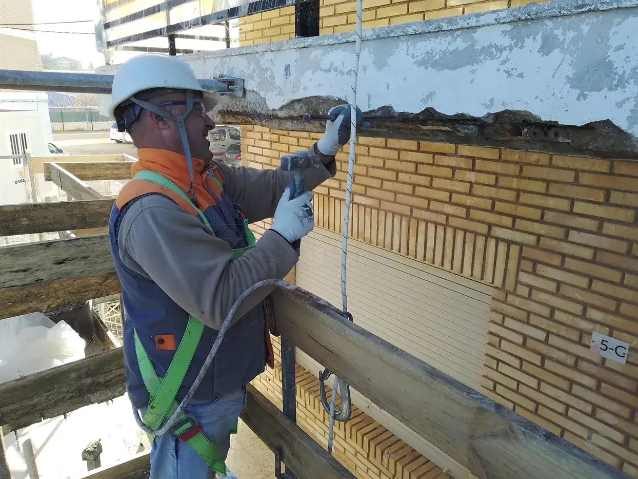 Obrero en andamio repara fachada dañada por humedad por filtración.