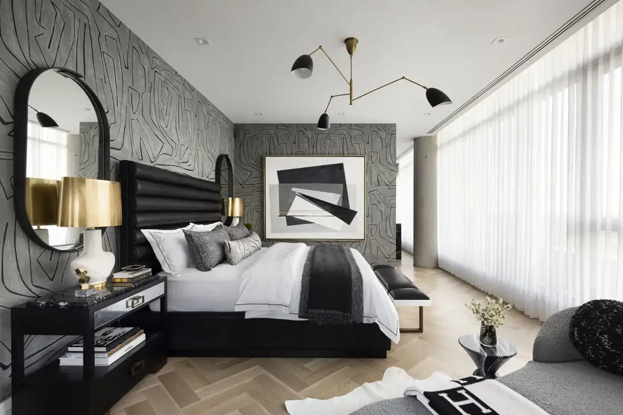 Elegante decoración de dormitorio con papel tapiz texturizado, cama negra, arte abstracto y lámparas doradas.