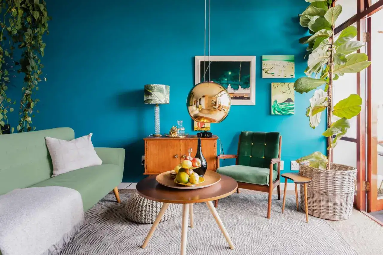 Ideas de colores para pintar un salón: pared azul turquesa vibrante, sofá verde menta, sillón verde esmeralda, detalles dorados y madera.