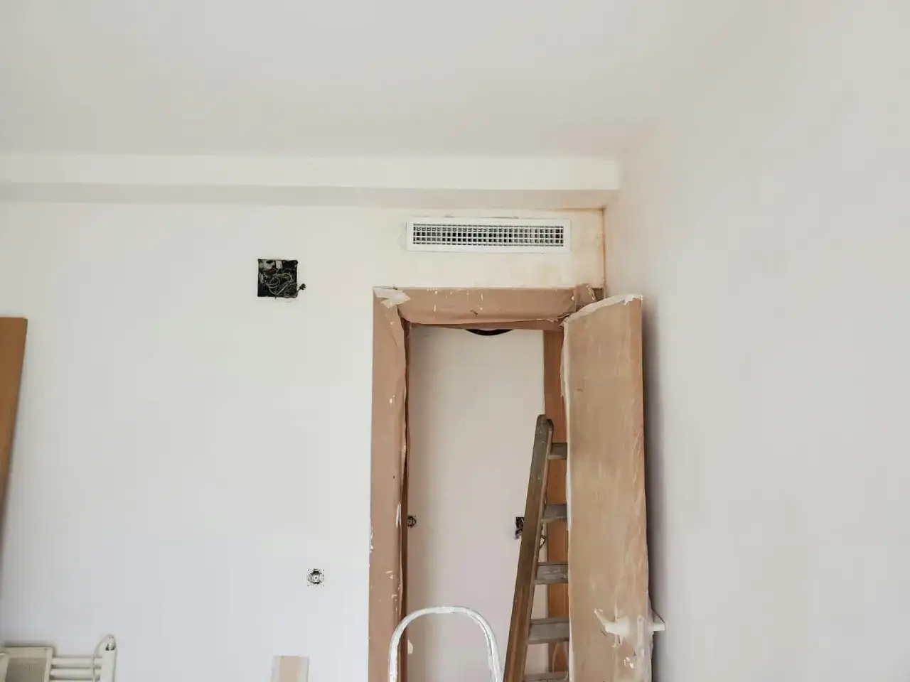 Habitaci&oacute;n en obra con rejilla de preinstalaci&oacute;n aire acondicionado en la pared, puerta abierta y escalera.