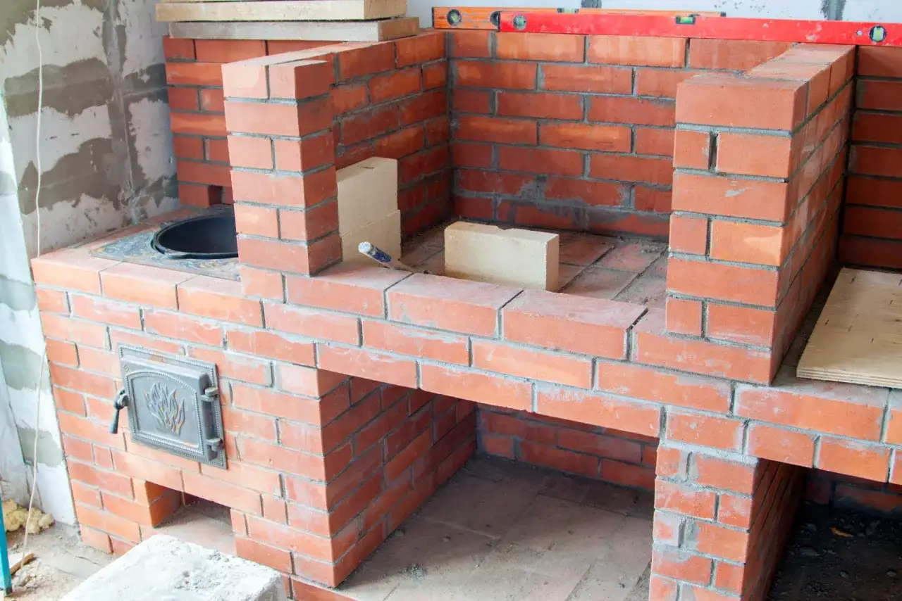 Construcción de una chimenea de obra con ladrillos rojos. Se aprecian los materiales y herramientas para como hacer una chimenea de obra.