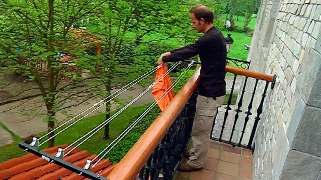 Hombre colgando ropa naranja en un tendedero exterior instalado en un balc&oacute;n.