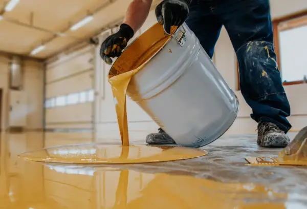 Hombre con guantes vierte pintura amarilla de un cubo para pintar suelo cocina.