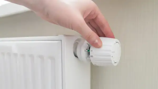 Mano ajustando el termostato para poner calefacción en casa. El radiador blanco está listo para calentar.