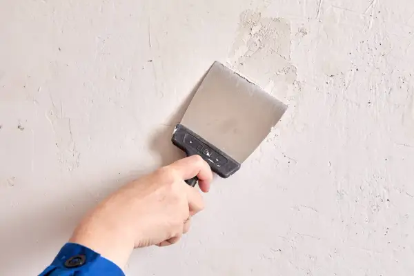 Mano con espátula aplica masilla a una pared irregular.