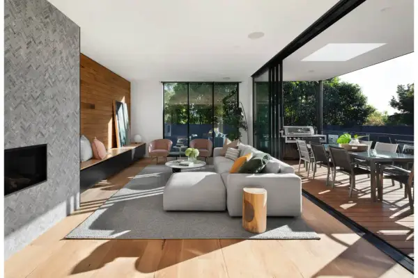 Elegante diseño de salas con chimenea de piedra, sofá modular gris, sillas rosadas y acceso a terraza con comedor exterior.