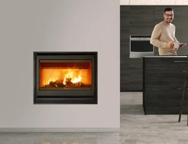 Chimenea cassette con fuego encendido. Un hombre sonríe con una taza y una tablet en una cocina moderna.
