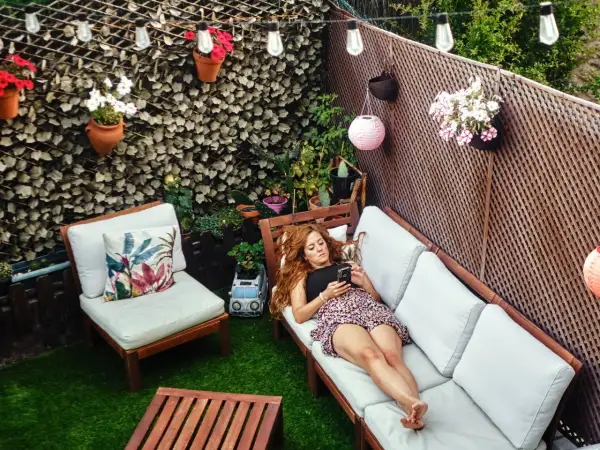 Mujer relajada en un sofá en un patio con césped artificial, luces y plantas. Ideas para decorar patio sin dinero.