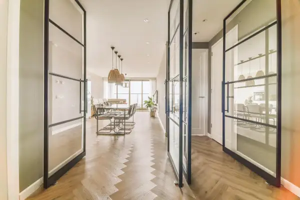 Amplio salón comedor rectangular de 25 metros, con suelo de espiga y separadores de cristal.