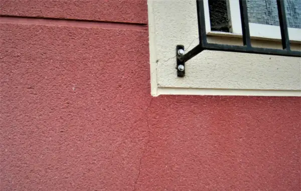 Detalle de juntas de dilatación en fachadas de color rojo y crema, con una ventana enrejada.