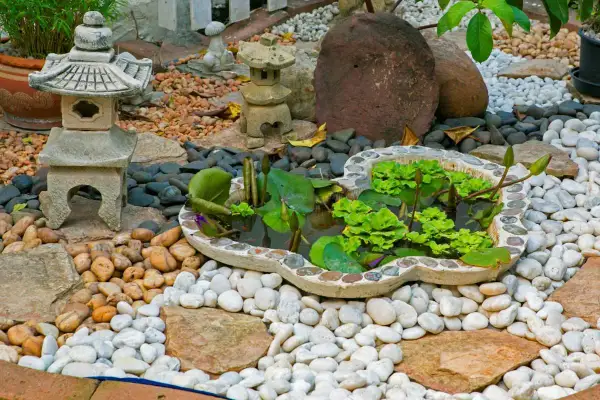 Un sereno jardín zen japonés con un estanque de lotos, linternas de piedra y rocas de diferentes tamaños.