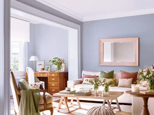 Ideas para decorar casa con poco dinero: sala acogedora con escritorio de madera, sofá blanco, cojines coloridos y flores frescas.